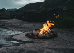 fire on black sand near body of water during daytime